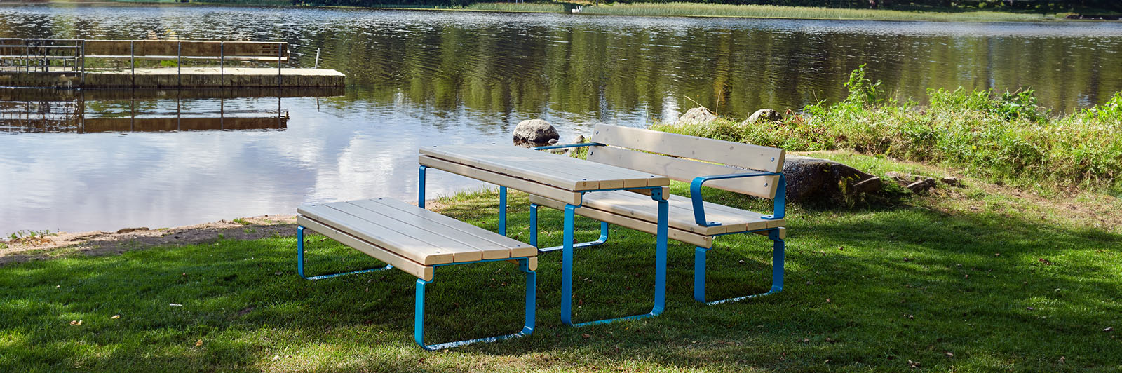 Wooden park table and benches with blue frames, settled against a natural background, with a lake.